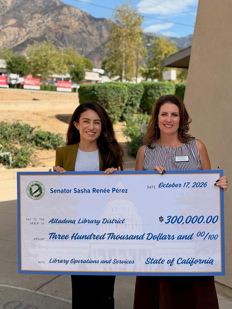 Senator Pérez standing outside next to library director both holding oversized check