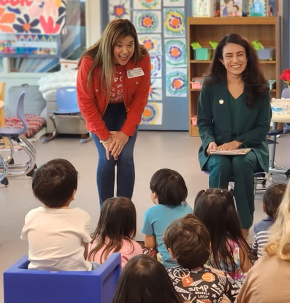 A smiling Senator Sasha Renee Perez sits in an elementary school classroom facing the students as she reads a book for Read Across America Day. 